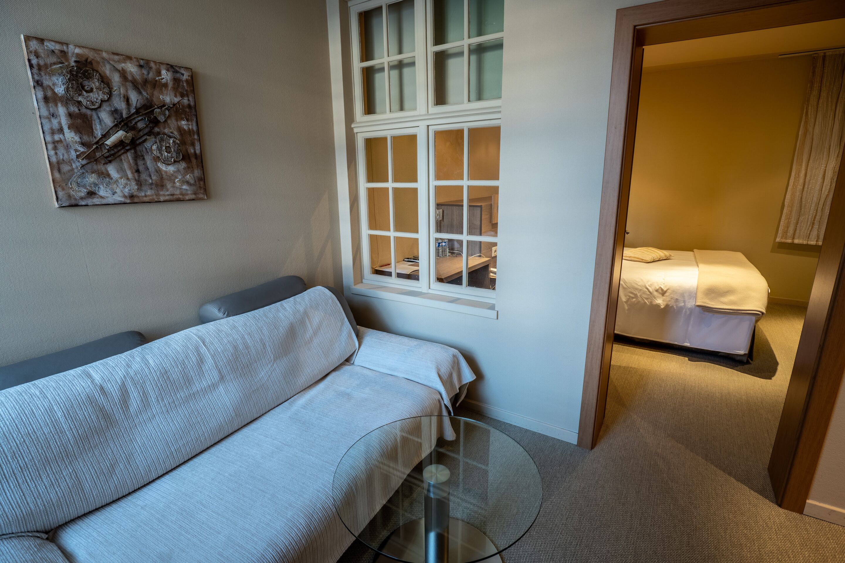 Ein modernes Zimmer mit einer Couch, einem Glastisch, einem Fenster und einem Bett.