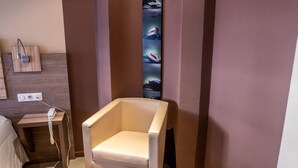 A modern hotel room with a wooden accent piece, a white armchair, and a small ottoman. - L'Ecrevisse (Wissembourg)