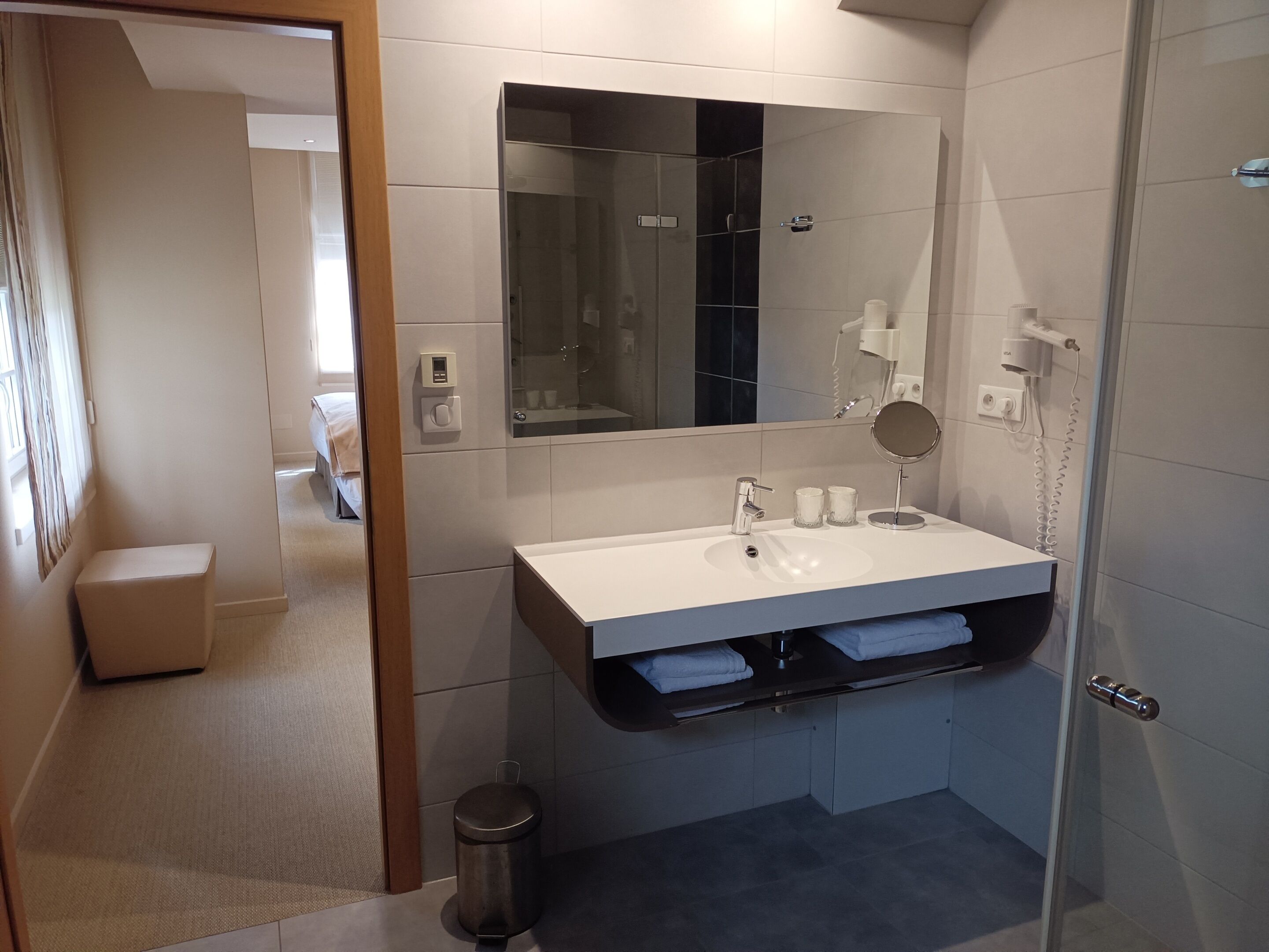 Ein modernes Badezimmer mit einem weißen Waschbecken, einem Spiegel und einer Duschkabine aus Glas.