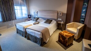 A modern hotel room with two beds, a large window with curtains, a wooden headboard, a small wooden side table, a white armchair, and a wall-mounted artwork. - L'Ecrevisse (Wissembourg)