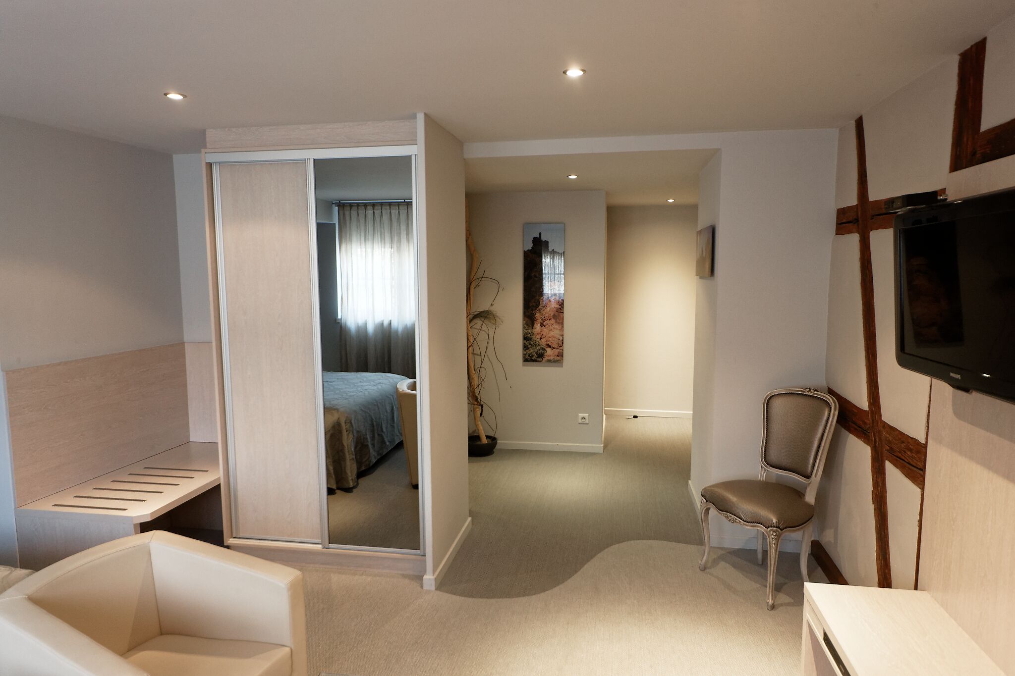 Une chambre d’hôtel moderne comprenant un lit, un coin salon avec un fauteuil, une télévision et une petite table.