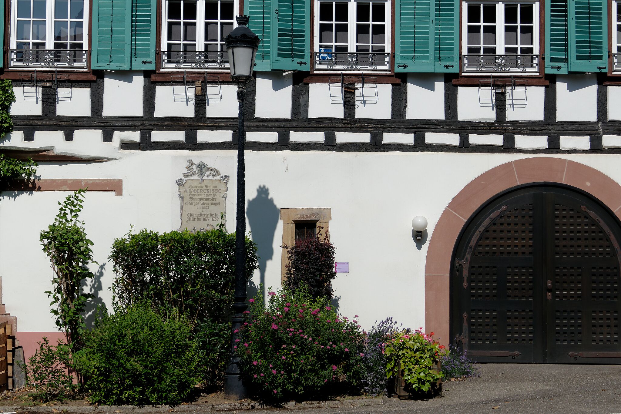 Un bâtiment à la façade blanche, aux volets verts et à la grande porte en arc de cercle.