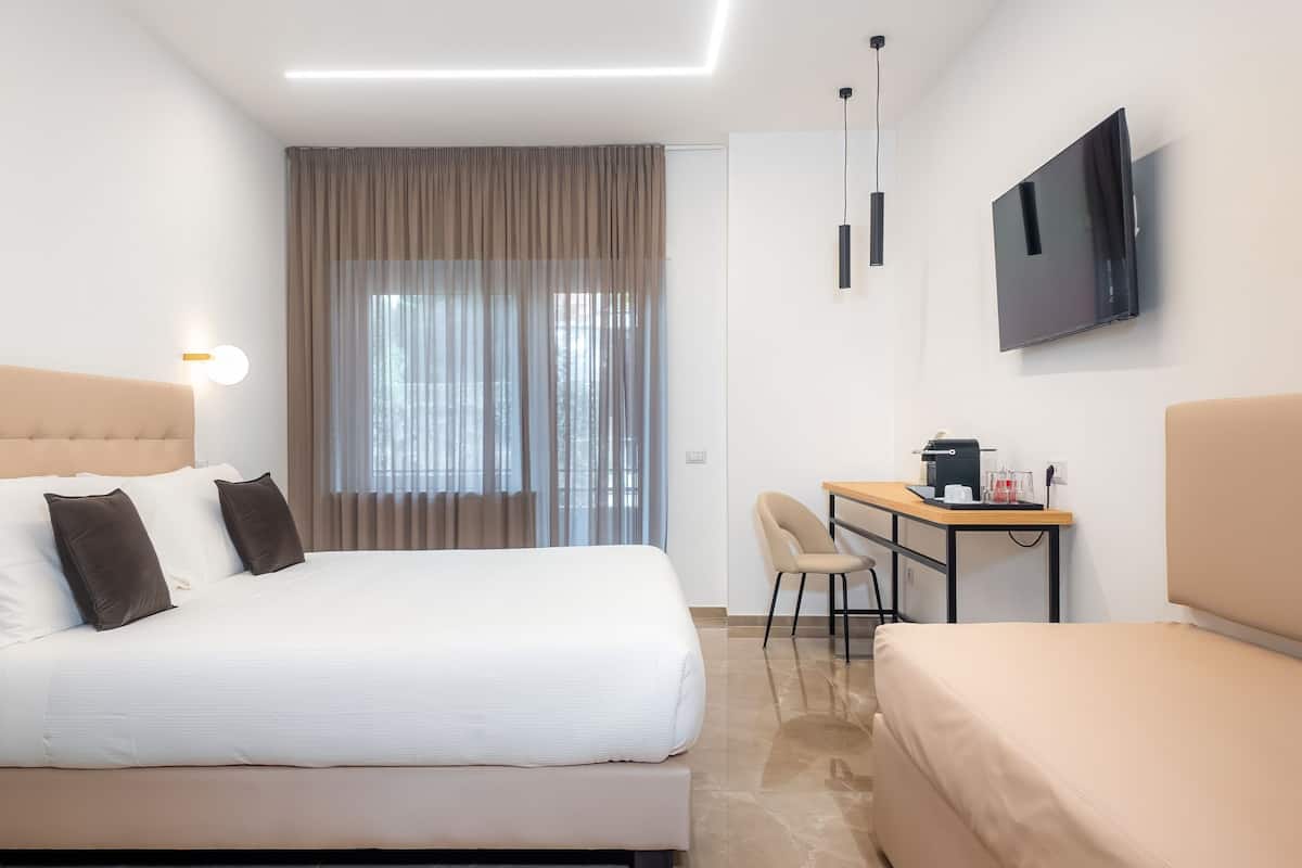 Habitación de hotel con cama, escritorio con silla, televisión y ventana con cortinas.