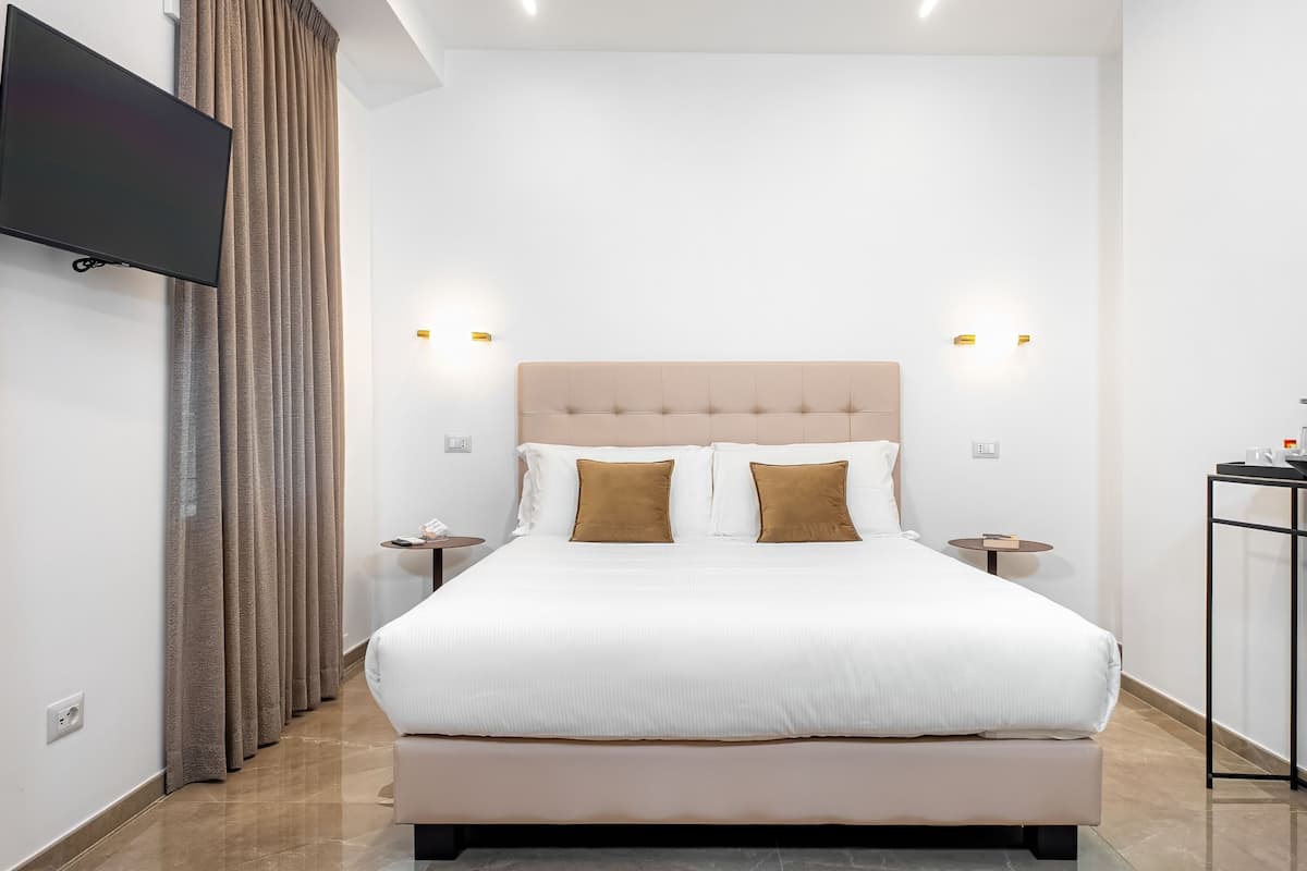 Una habitación de hotel moderna con una cama grande, mesitas de noche, un televisor de pantalla plana montado en la pared y una cafetera sobre una mesita auxiliar.