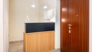 Un mostrador de recepción con encimera negra y base de madera, una puerta de madera con tirador de latón y dos lámparas colgantes sobre el mostrador.