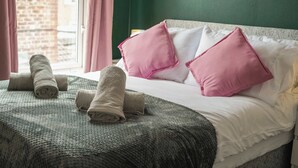 A neatly made bed with rolled towels, pink and white pillows, and a green wall.