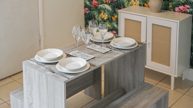 A dining table set with plates, glasses, and cutlery, with a cabinet in the background.