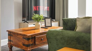 A wooden coffee table with a plant and a framed picture, a green armchair, and a TV displaying the Netflix logo.