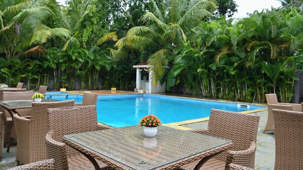 An outdoor pool area with wicker furniture and a small flower arrangement. - Vaarsa By Bay Hotels (Nagaon)
