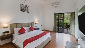 A hotel room with a large bed, two bedside tables, a ceiling fan, a wall-mounted TV, and a balcony with outdoor furniture. - Vaarsa By Bay Hotels (Nagaon)