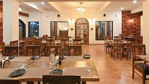 A spacious dining area with multiple tables and chairs, a chandelier, and a brick accent wall. - Vaarsa By Bay Hotels (Nagaon)