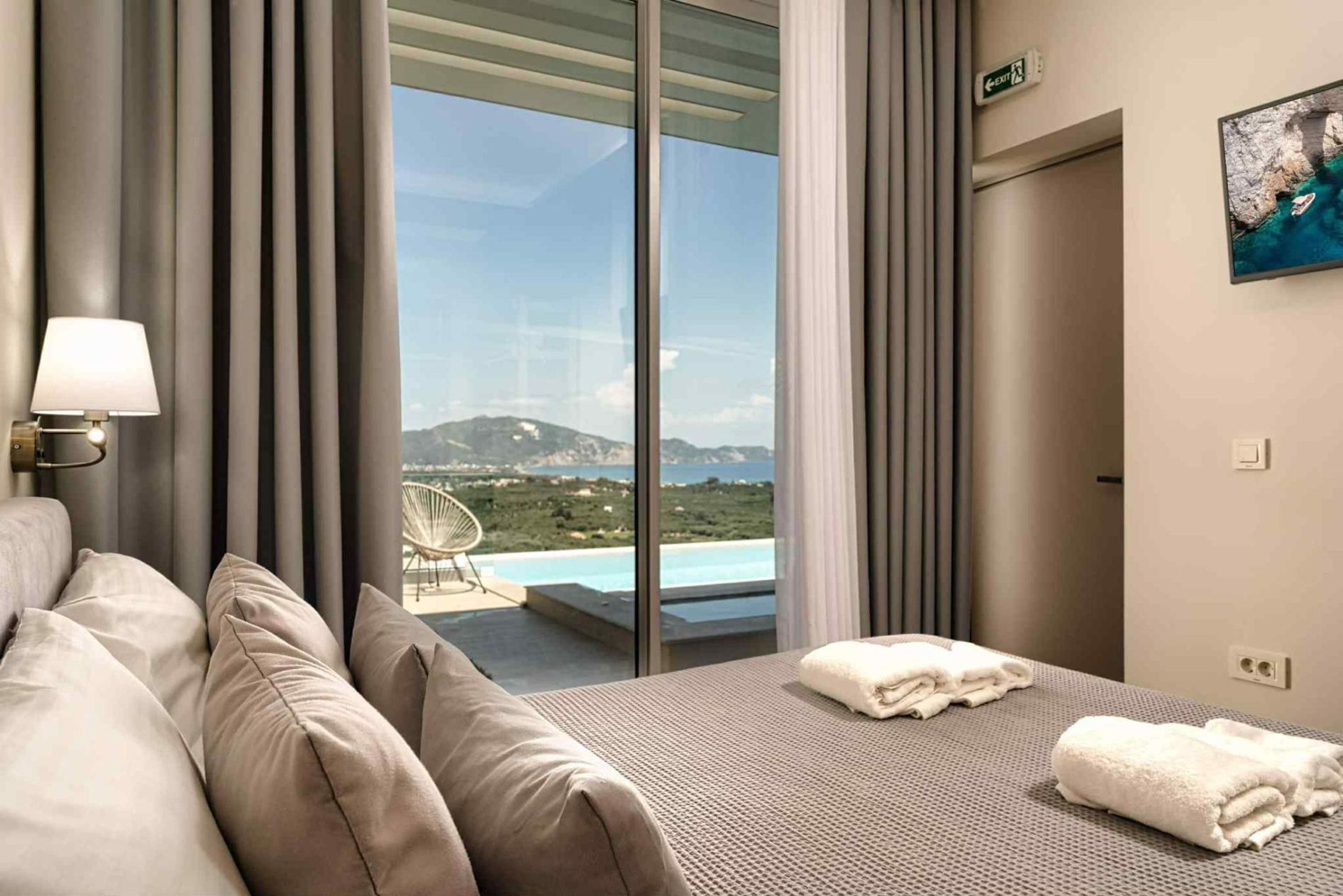 A hotel room with a bed, a chair, and a view of a pool and mountains.