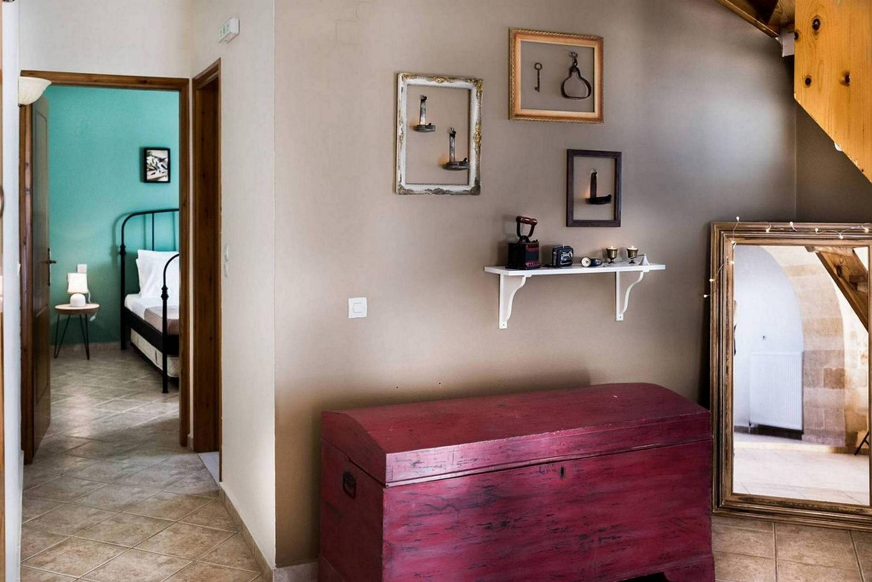 Quarto com cama, cómoda vermelha, estante branca com objetos e um espelho.