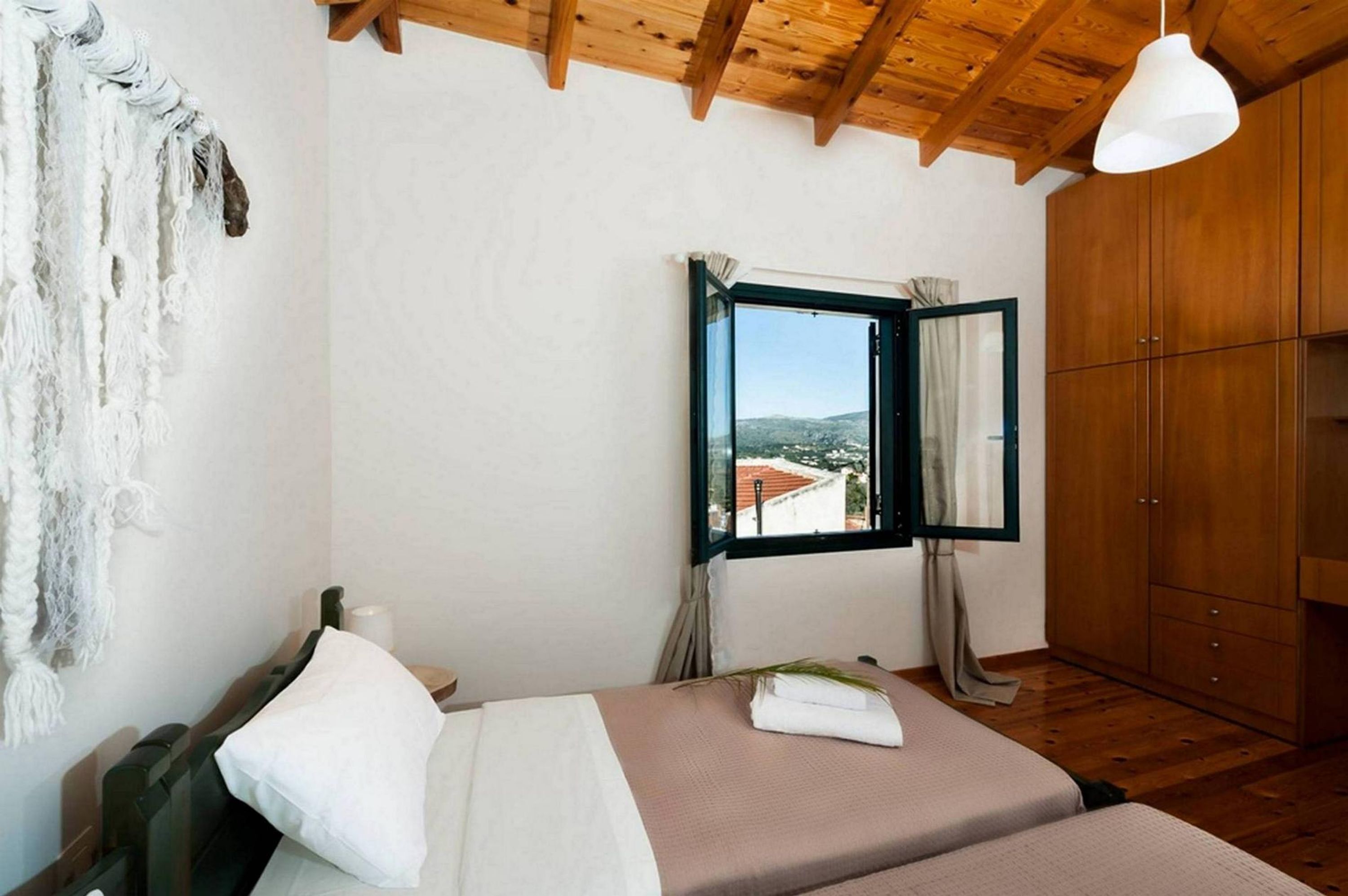 Ein Schlafzimmer mit Bett, Fenster mit Blick, Holzbalken an der Decke und einem Kleiderschrank.