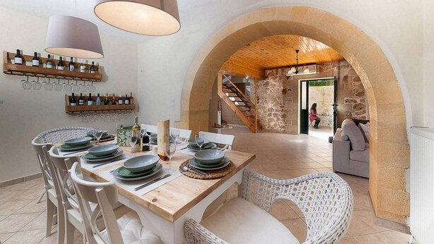 A dining area with a wooden table set for four, a stone archway, and a staircase leading to another level. - Villa Kirke in Chania (Apokoronas)