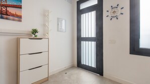 Un couloir avec une porte à cadre noir, une pancarte de bienvenue, un tableau représentant un paysage urbain encadré et un meuble avec des tiroirs.