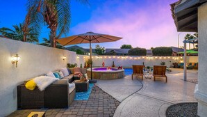 An outdoor patio area with a hot tub, lounge chairs, and string lights. - Desert Fun 4BR Retreat | Pool, Jacuzzi & Game Room (Bermuda Dunes)