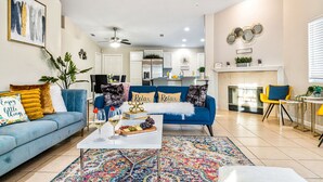 A modern living room with a blue sofa, a coffee table with a fruit platter, and a colorful rug. - Desert Fun 4BR Retreat | Pool, Jacuzzi & Game Room (Bermuda Dunes)