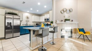 A modern kitchen with a central island, bar stools, and a yellow chair. - Desert Fun 4BR Retreat | Pool, Jacuzzi & Game Room (Bermuda Dunes)