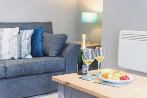 A room with a grey sofa, a bottle of champagne, two glasses, and a plate of food on a wooden table.