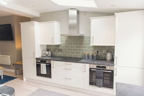 A modern kitchen with white cabinetry, a black countertop, and a green-tiled backsplash.