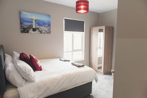 Un dormitorio con cama, almohadas, una ventana, un armario y un cuadro en la pared.