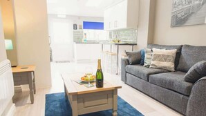 Ein modernes Wohnzimmer mit einem grauen Sofa, einem Couchtisch aus Holz mit Flasche und Gläsern sowie einem blauen Teppich.