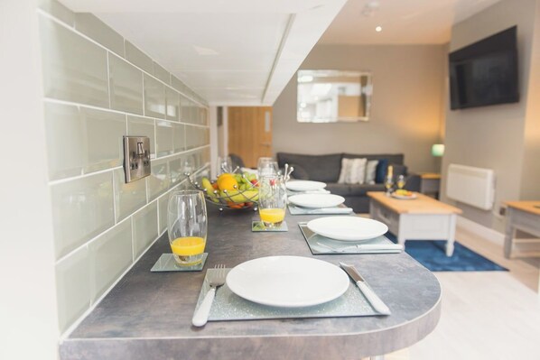 A modern kitchen with a curved countertop, a dining area with a sofa, and a TV mounted on the wall.