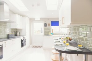 A modern kitchen with white cabinetry, a black countertop, and a breakfast setup with plates, glasses, and orange juice.