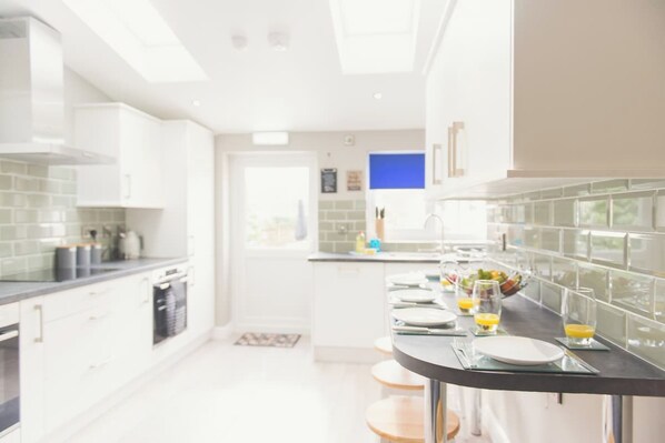 Cocina moderna con armarios blancos, encimera negra y una zona de desayuno con platos, vasos y jugo de naranja.