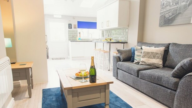 A living room with a grey sofa, a wooden coffee table with a bottle and glasses, and a blue rug. - Modern Town Centre House w/ En-Suites & Fast WiFi (Tamworth)