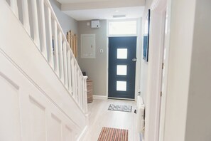 A hallway with a staircase, a dark door, and a light-colored floor.
