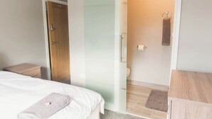 Ein Hotelzimmer mit einem Bett, einem Nachttisch aus Holz, einem Badezimmer mit Toilette und einem Handtuchhalter.