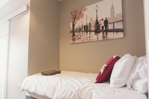 Ein Schlafzimmer mit einem Bett, Kissen, einem Gemälde von einem Paar auf einer Brücke und einem Fenster.
