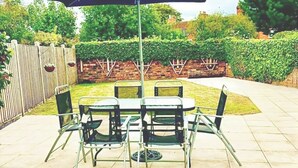A patio with a table and chairs, a large umbrella, and a brick wall with a wooden fence. - Modern Town Centre House w/ En-Suites & Fast WiFi (Tamworth)
