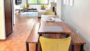 A spacious living area with a wooden dining table, yellow chairs, a sofa, and a TV mounted on the wall. - Experience a perfect vacation in our newly renovated 3-bedroom townhome in Playas Del Coco (Playas Del Coco)