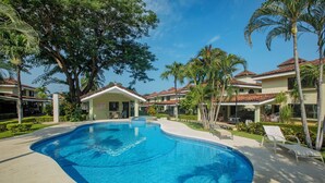 A swimming pool surrounded by palm trees and lounge chairs, with a building in the background. - Experience a perfect vacation in our newly renovated 3-bedroom townhome in Playas Del Coco (Playas Del Coco)
