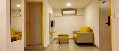 A hallway with a mirrored wall, a door, a small table, a sofa, and an air conditioning unit.