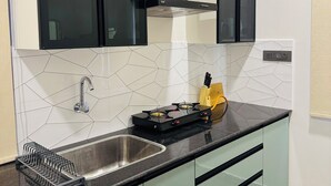 Une cuisine dotée d’un évier en acier inoxydable, de meubles de rangement noirs, d’une cuisinière à gaz et d’un conduit de ventilation.