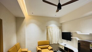 Un espace de vie compact comprenant un canapé, un fauteuil, un ventilateur de plafond, une télévision et un réfrigérateur.