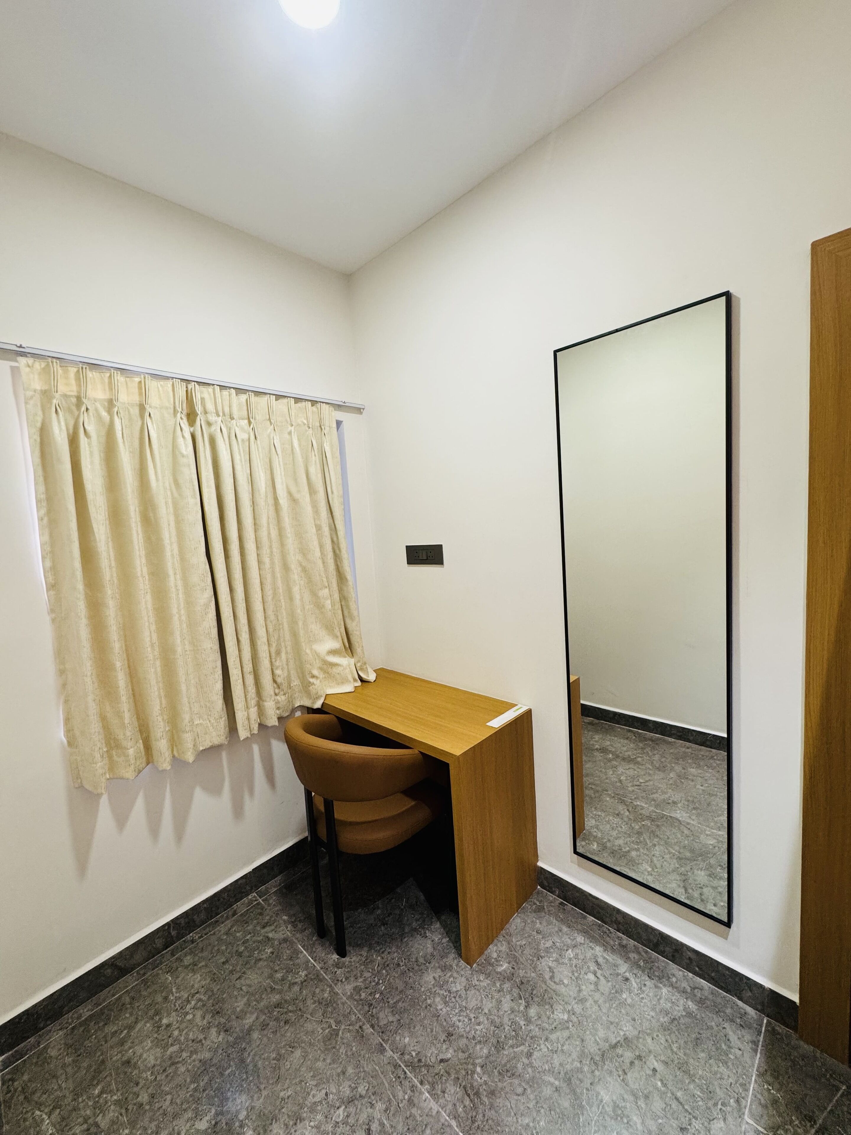 A small, private office with a desk and chair, a large mirror, and a curtained window.