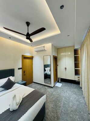 Une chambre d’hôtel moderne équipée d’un lit, d’un ventilateur de plafond, d’une armoire et d’un miroir.