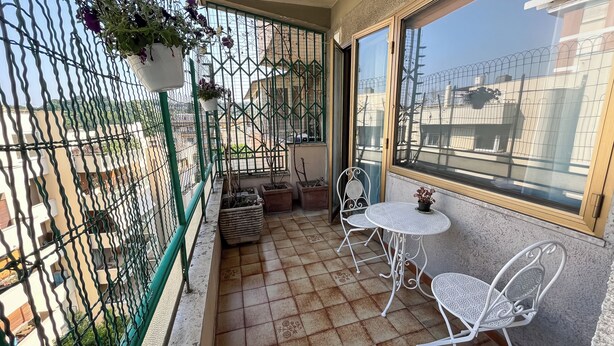 A balcony with a tiled floor, two white metal chairs, a small round table, and a potted plant.