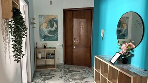 A hallway with a wooden door, a marble floor, a wooden console table with papers, a mirror, and a wall with a painting.