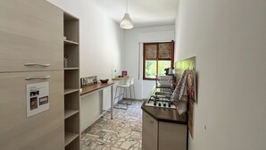 A narrow kitchen with a tiled floor, wooden cabinets, a gas stove, and a window with blinds.