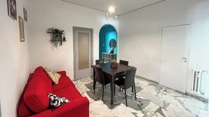 A modern living room with a red sofa, a dining table with chairs, a kitchen area with a blue arch, and a white door.