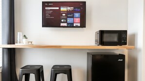 Een kitchenette met een zwarte koelkast, een magnetron en een tv aan de muur met verschillende apps.
