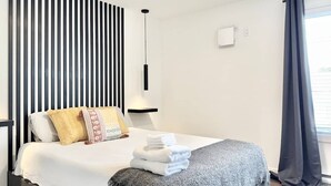 Een moderne hotelkamer met een bed, nachtkastje, wandlamp en een raam met gordijnen.