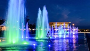 A nighttime scene with a water fountain display featuring multiple jets of water illuminated by colorful lights. - Lévis Center | New Studio with Queen Bed + A/C (Levis)