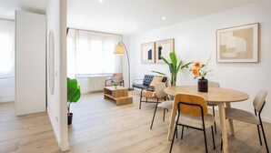 Un salon moderne avec un coin repas, comprenant un canapé, des fauteuils, une table basse et une grande fenêtre.